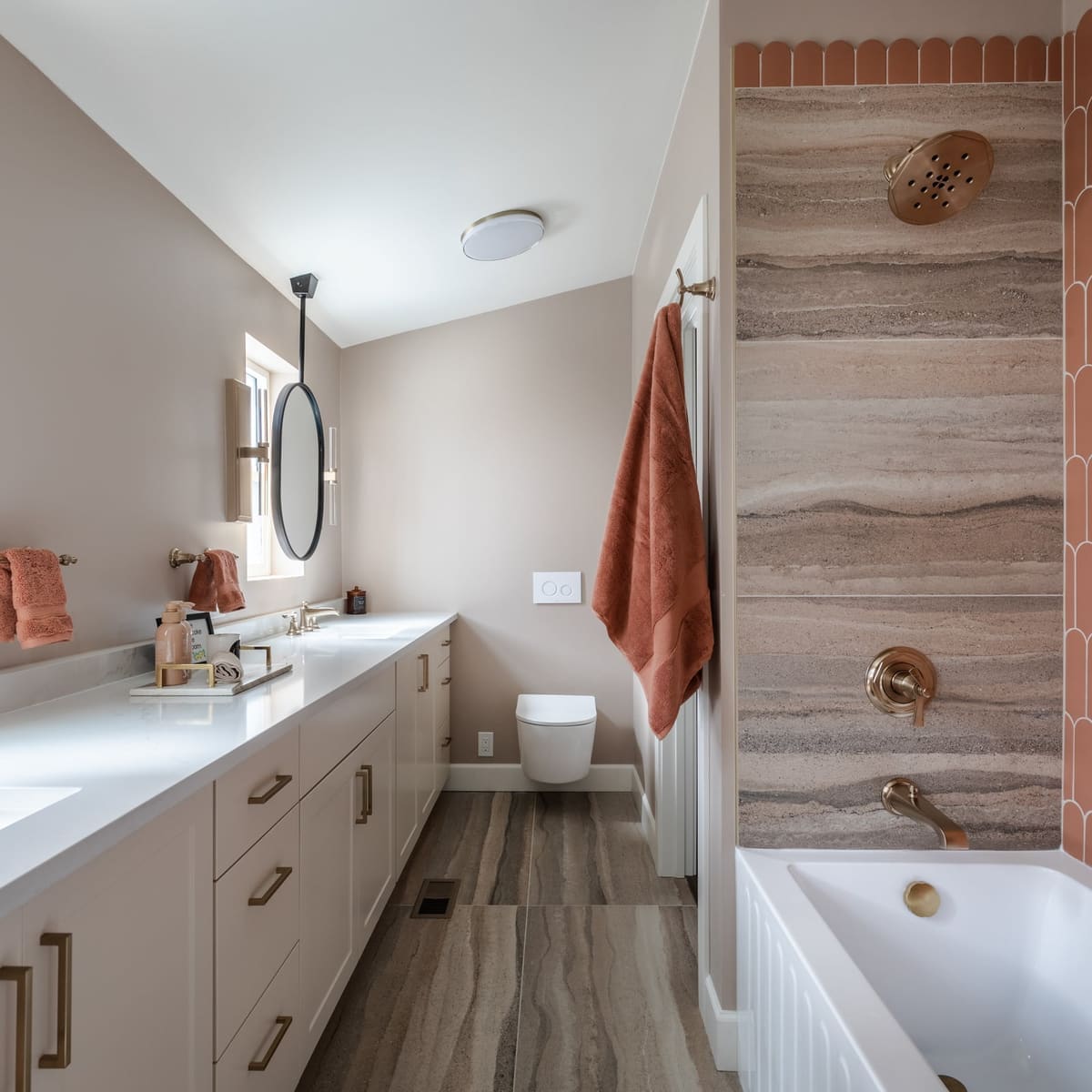 Bathroom with a long double vanity, wall-hung toilet and tub framed in terracotta fan tile and striated porcelain