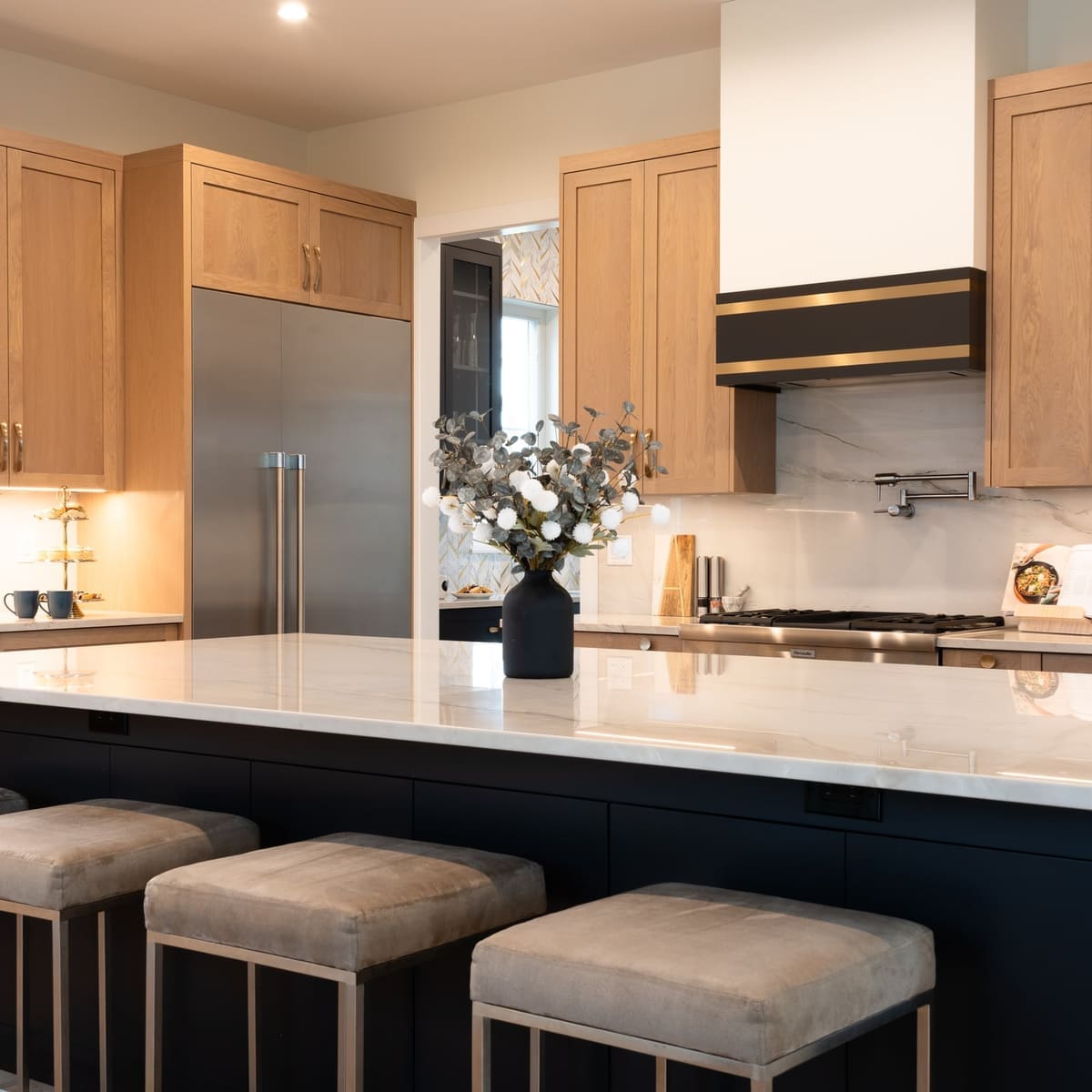 Navy kitchen island with white quartz and four upholstered stools facing white oak cabinetry