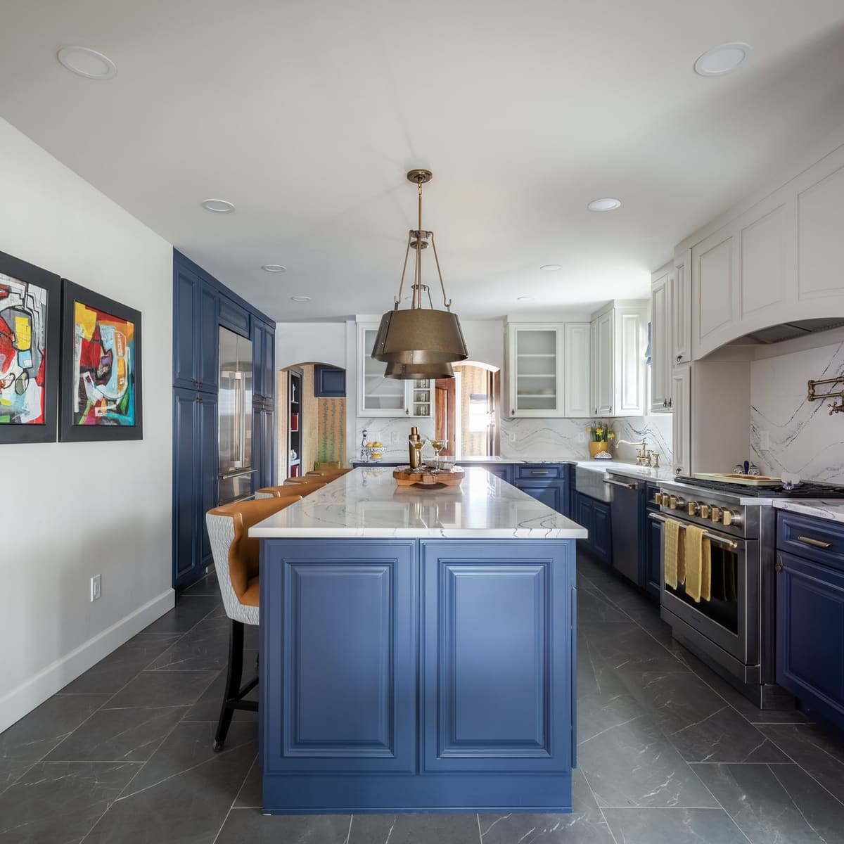 Navy island with brass dome pendants and white quartz in a kitchen hung with colorful framed art