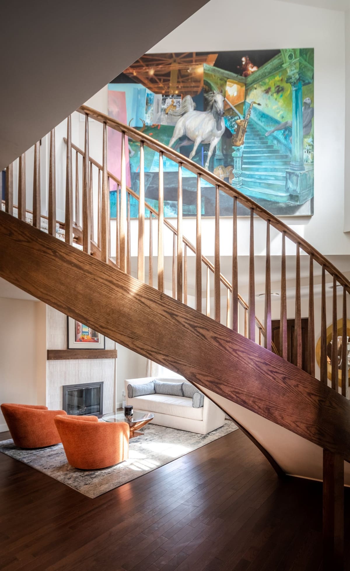 Curved wood staircase with slender balusters and a patterned runner, framing a living room with orange chairs